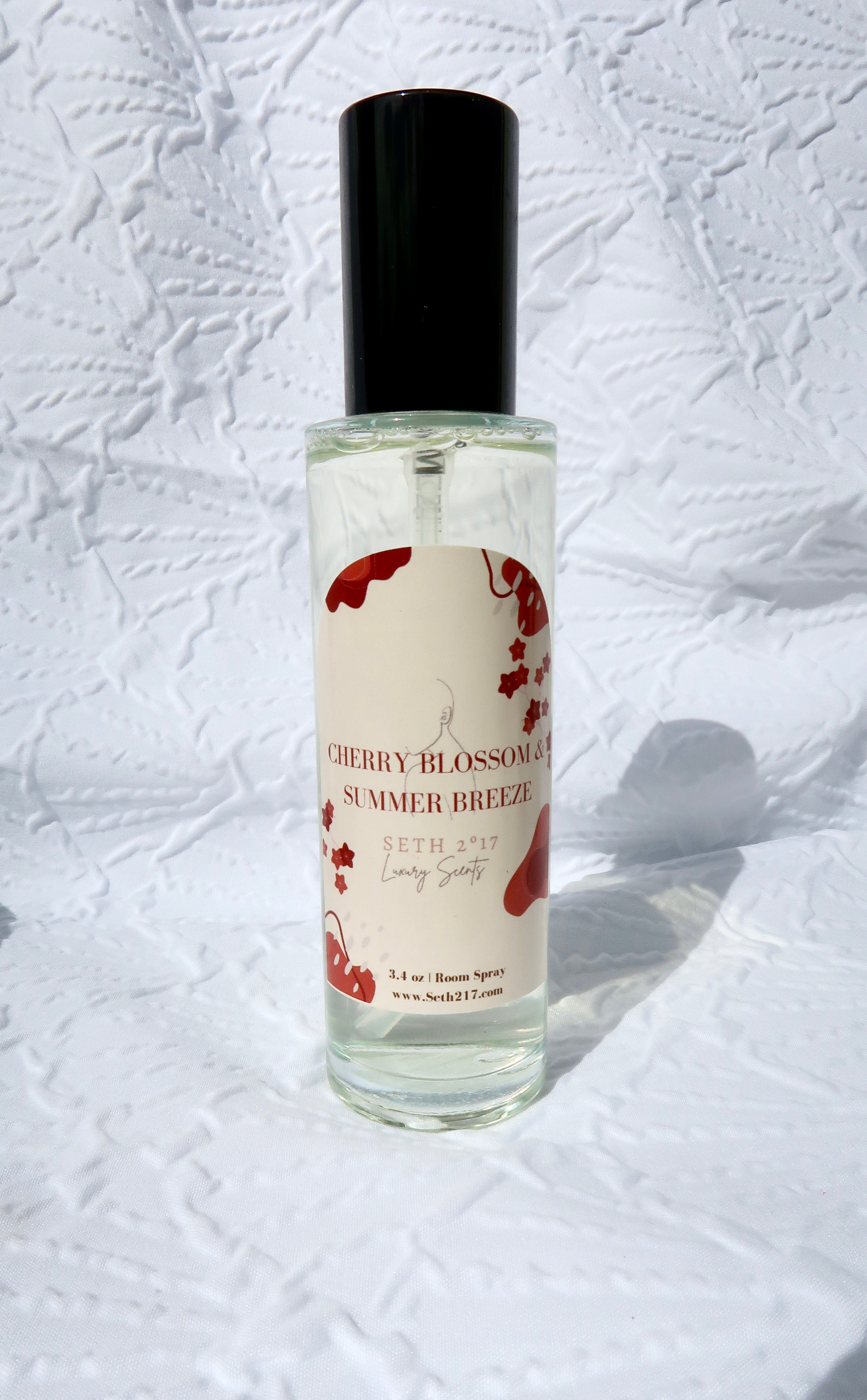 Two room spray bottles with labels, one labeled 'CHERRY BLOSSOM & SUMMER BREEZE' and the other 'ASHMERE & VANILLA'. The bottles are placed on a textured surface.