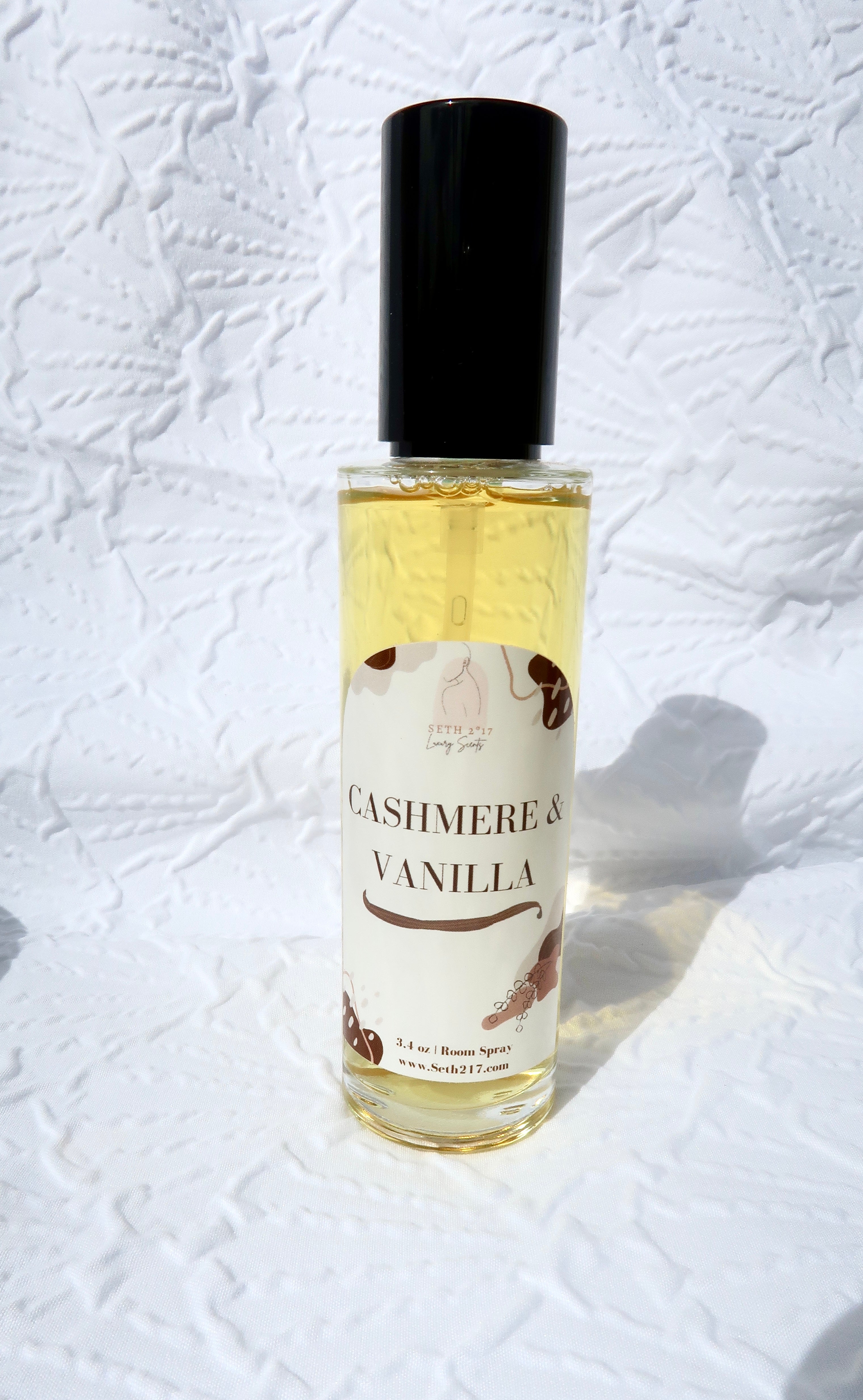 Two room spray bottles with labels, one labeled 'CHERRY BLOSSOM & SUMMER BREEZE' and the other 'ASHMERE & VANILLA'. The bottles are placed on a textured surface.