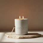 Candle in a white container with 'Seth 217' branding on a wooden board against a beige background
