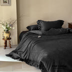 Black bedding set on a bed in a bedroom with a vase of flowers on a side table.