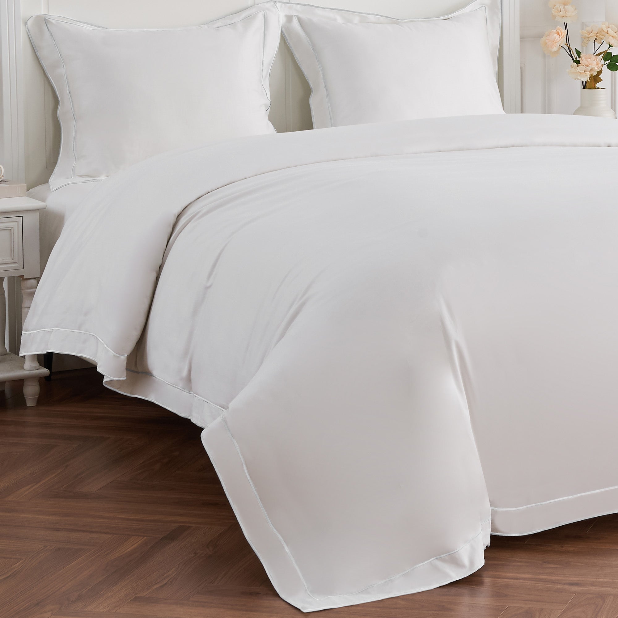 White bedding set on a bed with a wooden floor and side table in the background.